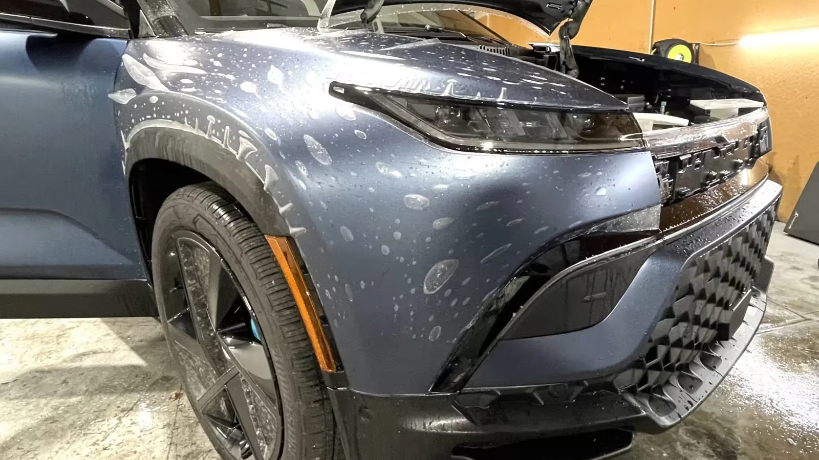 Clear paint protection film being aligned across a blue vehicle's front fender and bumper at APC Auto Spa